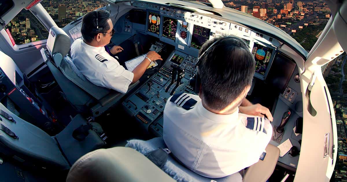 Two pilots in an airline cockpit during flight, with a city visible below