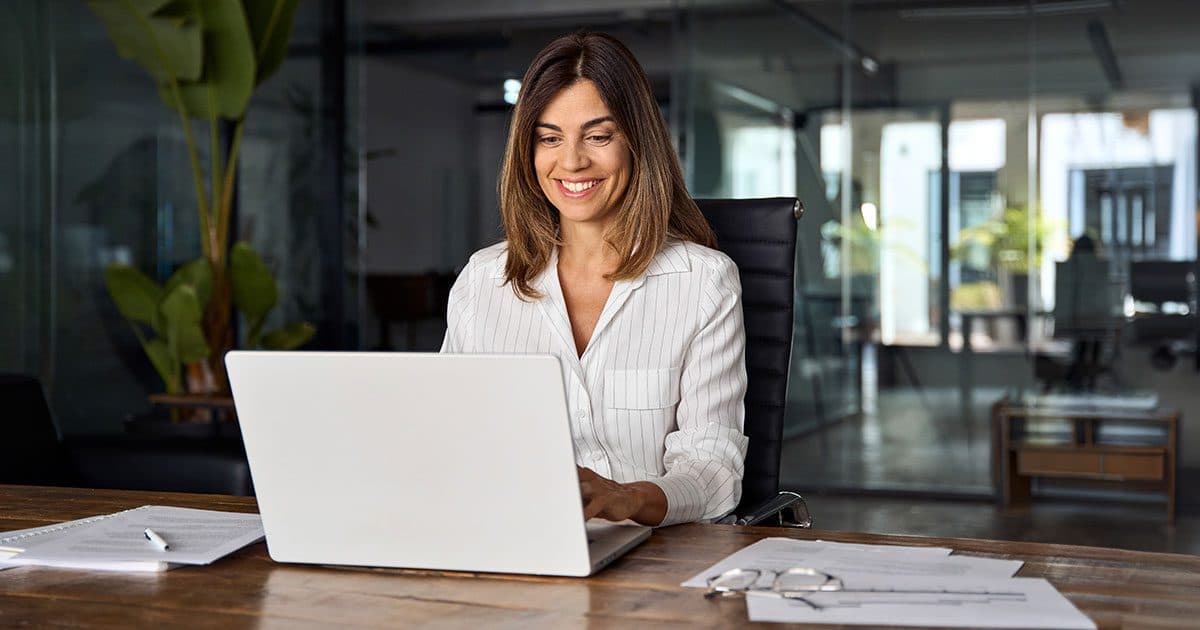 Smiling business owner working on a laptop in a modern office, representing tips for building an accounting software tech stack to streamline bookkeeping and financial management