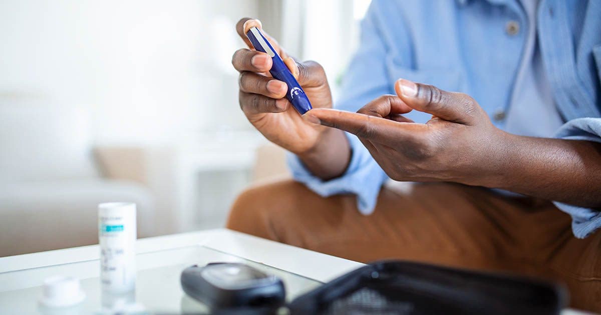 man sitting on sofa testing his glucose levels as he deals with chronic illness