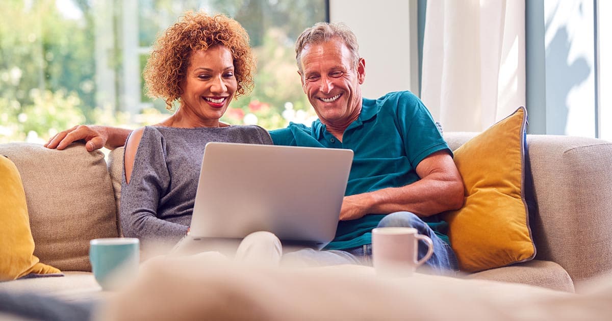 Mature couple smiling while reviewing investment and tax planning strategies on a laptop, representing an enhanced direct indexing approach for high-net-worth portfolios.