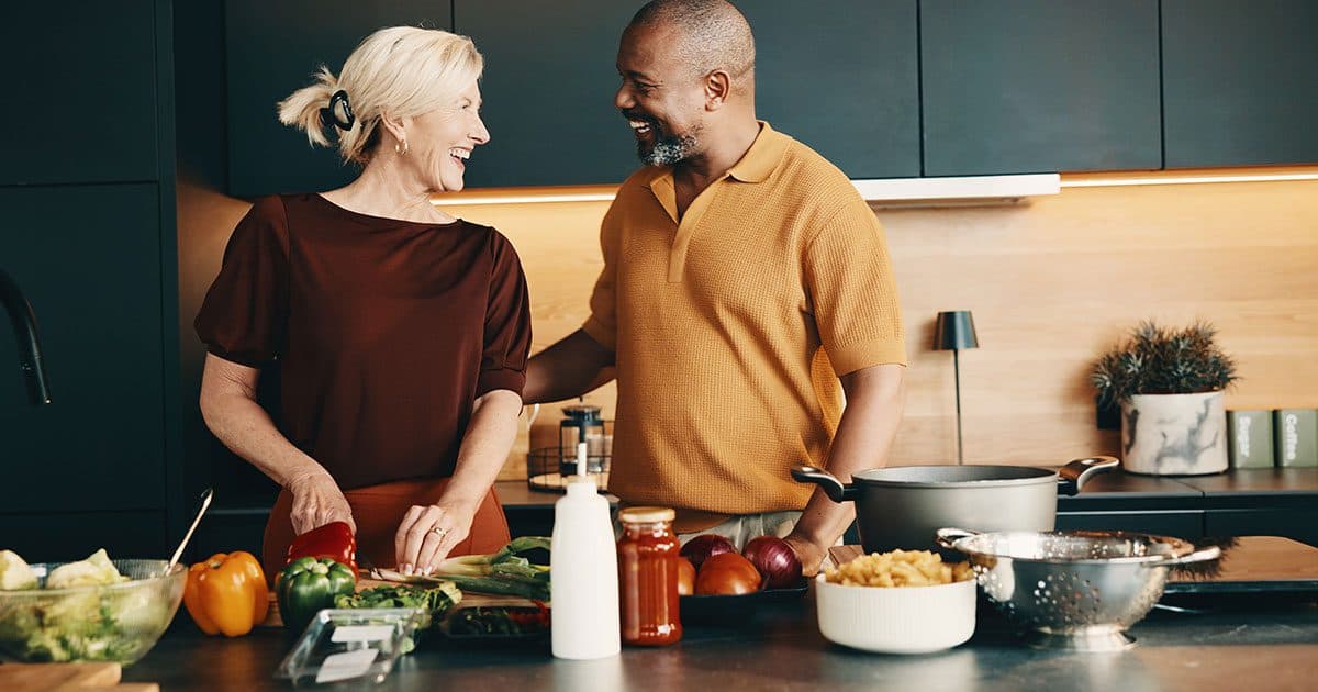 Couple laughing together while cooking in a modern kitchen, illustrating proactive tax planning strategies for long-term financial security.