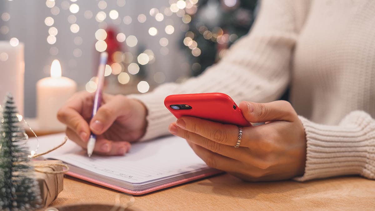 Woman's hands with pen and mobile phone writing out a checklist