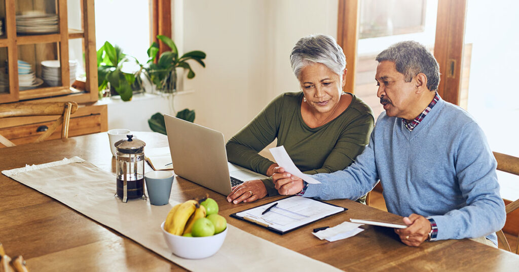 Mature couple looking at documents at dining room table with a laptop
