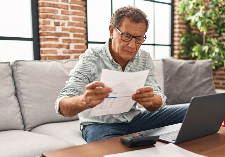 Middle aged man working on laptop and looking at documents.