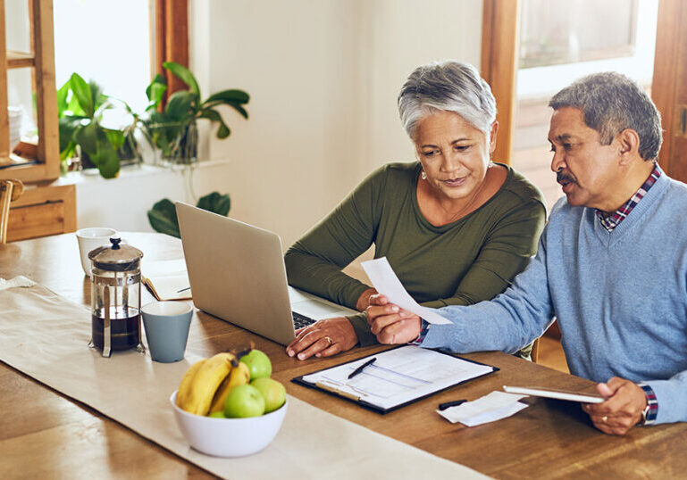 Mature couple looking at documents at dining room table with a laptop