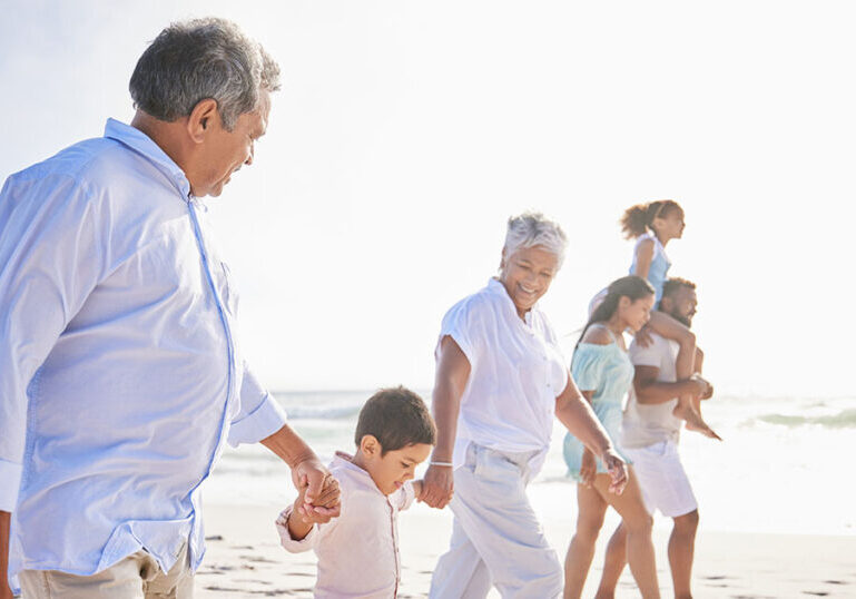 Multigenerational family holding hands walking on beach