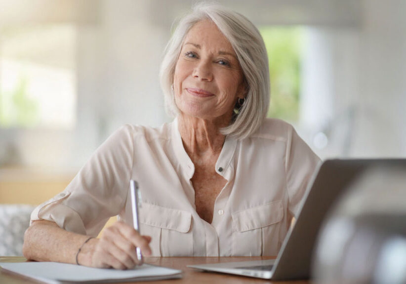 Mature woman writing at desk and smiling.