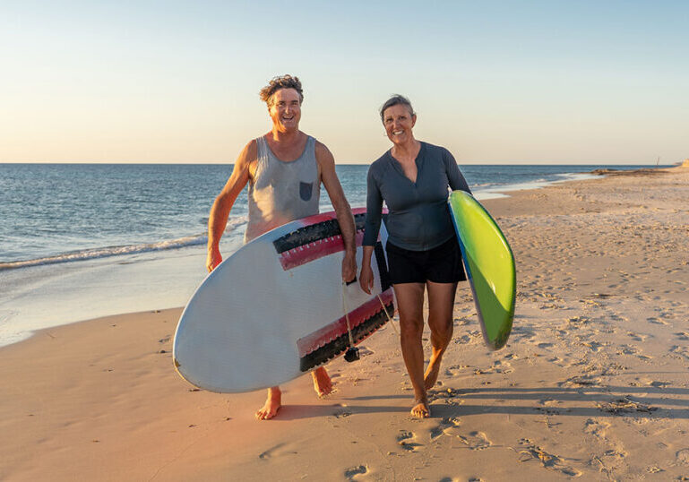 Couple holding surfboards walking on the beach.