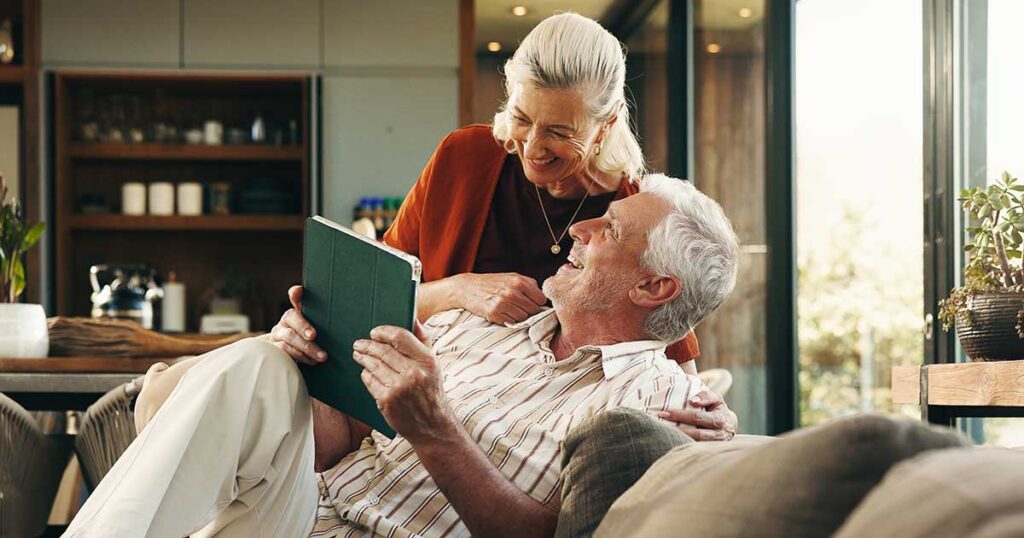 Retired couple relaxing together at home while reviewing information on a tablet, representing high-net-worth families using comprehensive estate planning to protect their legacy