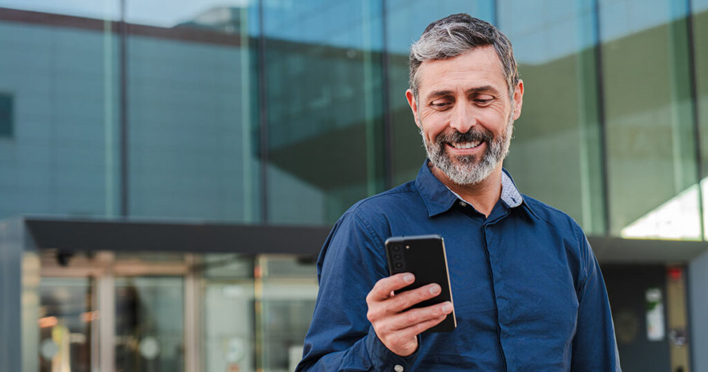Pre-retiree standing outside an office building checking his phone, symbolizing planning in the gray zone years 5 to 10 years before retirement