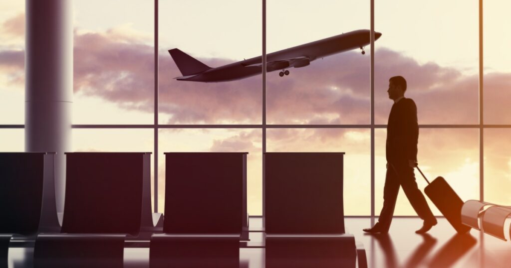 Business traveler walking through airport terminal with luggage as plane takes off at sunset