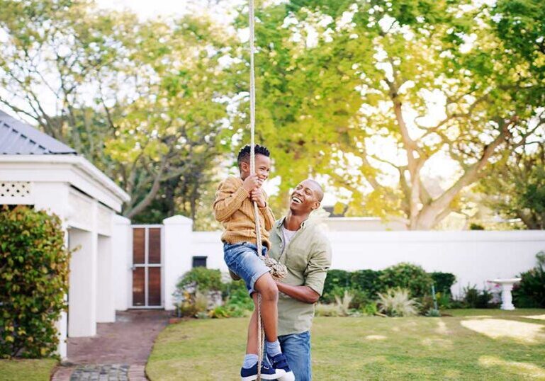 Father helping child swing on a rope in the backyard of a suburban home