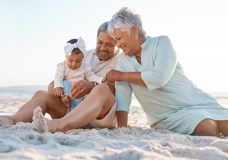 Grandparents sitting on the beach with their grandchild, symbolizing multigenerational wealth, legacy planning and the importance of thoughtful estate planning for wealthy families