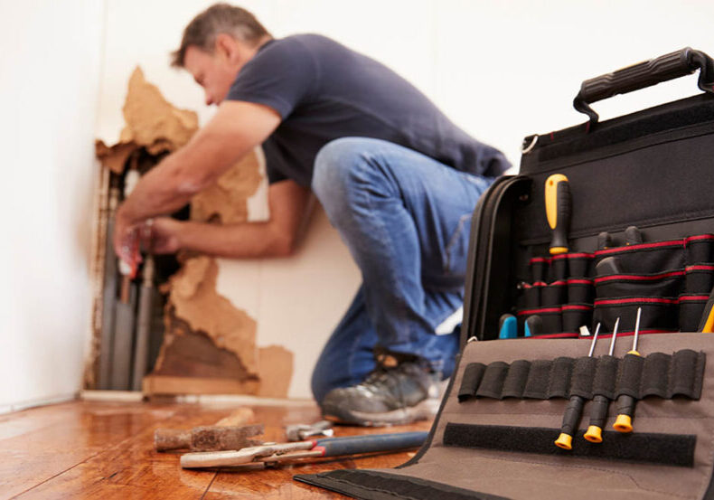 Man repairs a burst pipe in living room wall