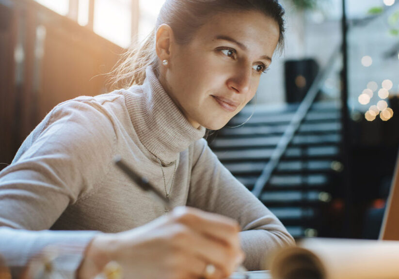 Woman taking notes as she reads good news on laptop