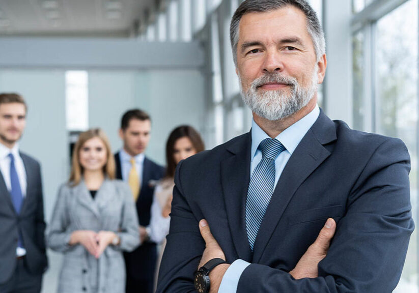 Senior businessman in office standing in front of the team