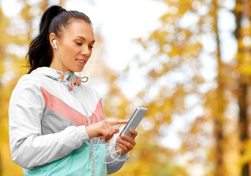 active woman in autumn park and looking at her phone