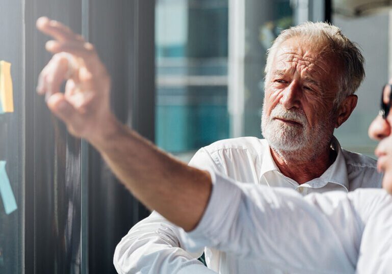 Two older professionals reviewing plans on a glass wall, representing how today’s millionaires take a more active, strategic approach to designing their retirement lifestyle