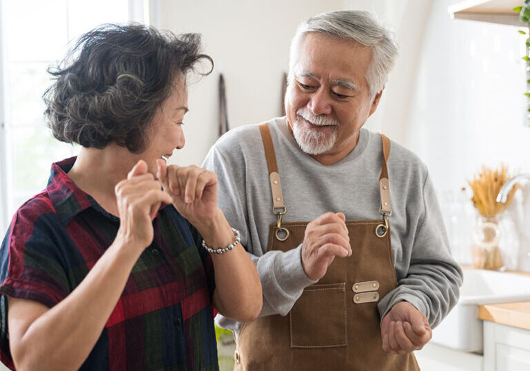 Asian mature senior couple is dancing and smiling in kitchen at home.