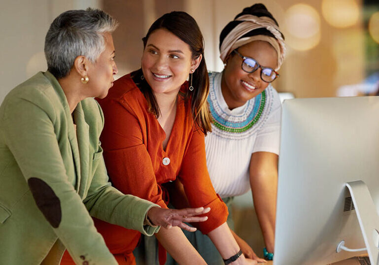 Collaboration, communication and a business woman with her team, working on a computer in the office at night. Teamwork, diversity and coaching with a senior female manager training her staff at work.