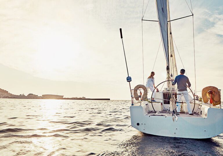 Couple standing on the deck of a sailboat at sunset, symbolizing protection and peace of mind on the water.