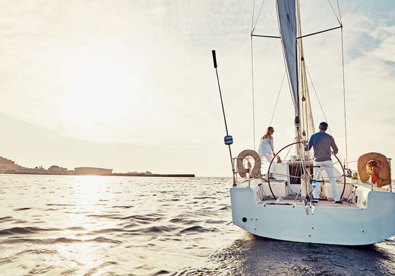 Couple standing on the deck of a sailboat at sunset, symbolizing protection and peace of mind on the water.