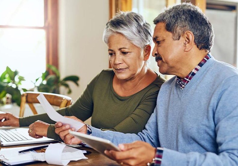 Senior couple, budget planning and health insurance checklist with computer at home. Documents, pension and elderly people with financial, tax and debt form in a house with bills and pc admin.