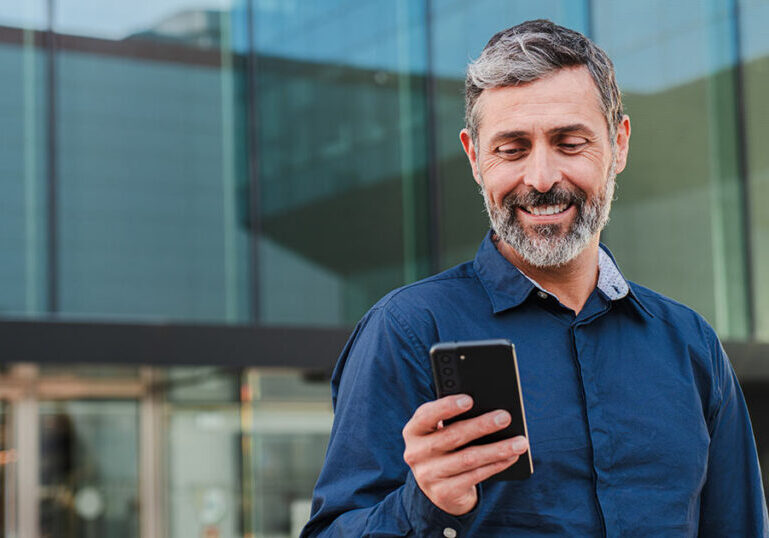 Pre-retiree standing outside an office building checking his phone, symbolizing planning in the gray zone years 5 to 10 years before retirement