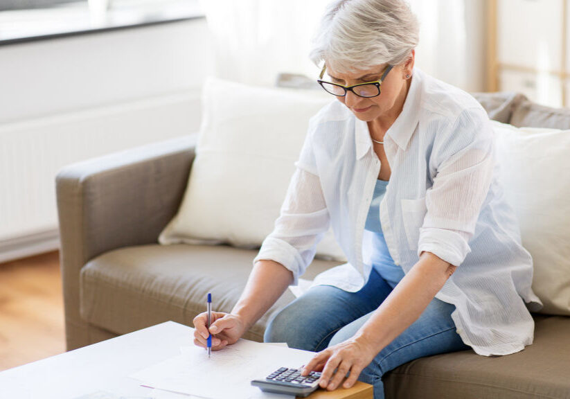 business, savings, annuity insurance, age and people concept - senior woman with papers or bills and calculator writing at home