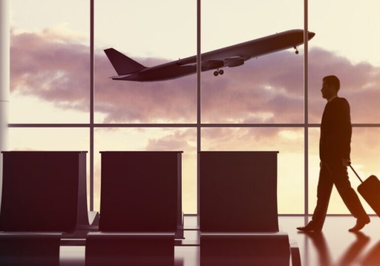 Business traveler walking through airport terminal with luggage as plane takes off at sunset